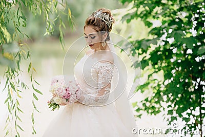 Portrait of a bride who walks in nature. The girl looks down and demonstrates her beautiful soft makeup and long Stock Photo