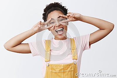 Portrait of bright carefree attractive dark-skinned woman with curly bun, showing peace signs over eyes and smiling Stock Photo