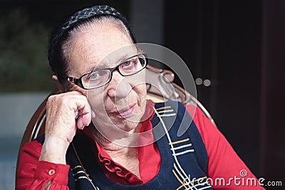 Portrait of a brooding old woman sitting on a chair and staring at the camera Stock Photo