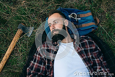 Portrait brutal bearded and moustached woodcutter hipster Gypsy man in the forest with ax. Man lying on the grass and dreams Stock Photo