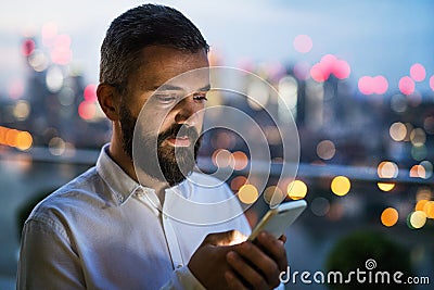A businessman with smartphone at sunset, text messaging. Stock Photo