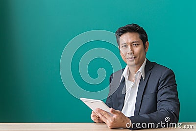 Portrait of businessman smiling and using pad at desktop against of blue wall. Stock Photo