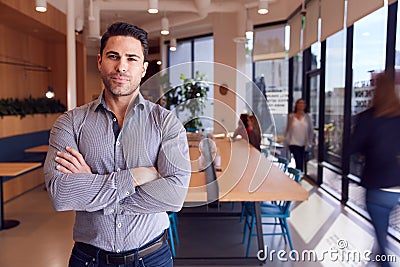 Portrait Of Businessman Standing In Busy Modern Open Plan Office With Colleagues In Background Stock Photo