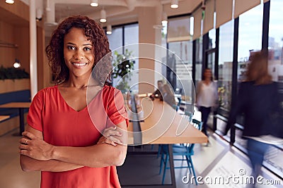 Portrait Of Businesswoman Standing In Busy Modern Open Plan Office With Colleagues In Background Stock Photo