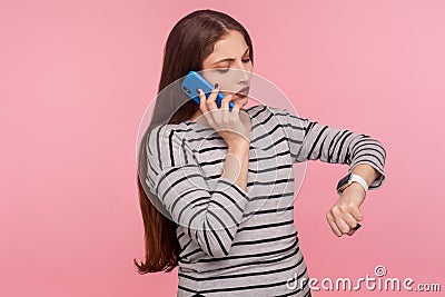 Portrait of busy, impatient, dissatisfied woman in striped sweatshirt talking on mobile phone checking time Stock Photo