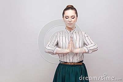 Portrait calm of beautiful young woman in striped shirt, green skirt with makeup and collected ban hairstyle, standing with closed Stock Photo