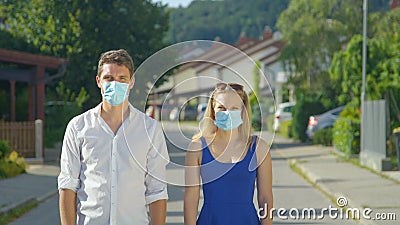 PORTRAIT: Caucasian couple wearing surgical facemasks stand in middle of street Stock Photo