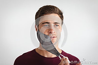 Portrait of caucasian man removing face mask against grey background Stock Photo