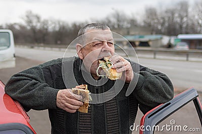 Caucasian senior driver gobbling lyulya kebab in lavash near his car Stock Photo
