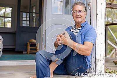 Portrait of caucasian senior man dressed in casuals sitting on steps outside cottage Stock Photo
