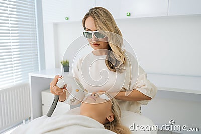 Portrait of certified cosmetologist wearing protective glasses conducting facial rejuvenation using modern apparatus for Stock Photo