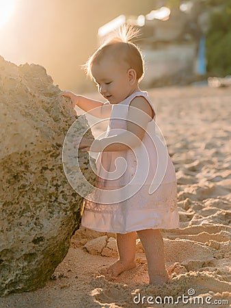 Portrait of charming baby girl in dress on sandy beach with sunset tones Stock Photo