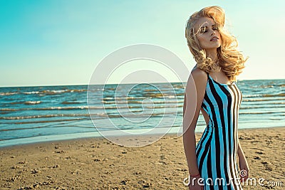 Portrait of a charming blond long-haired woman in long black and white striped dress smelling and enjoying aroma of the sea Stock Photo