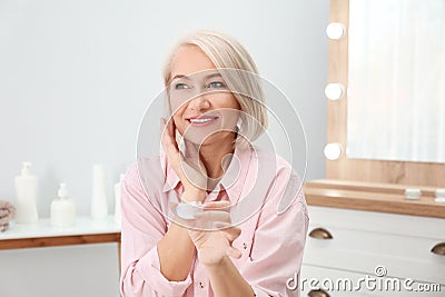 Portrait of charming mature woman with healthy beautiful face skin and natural makeup applying cream Stock Photo