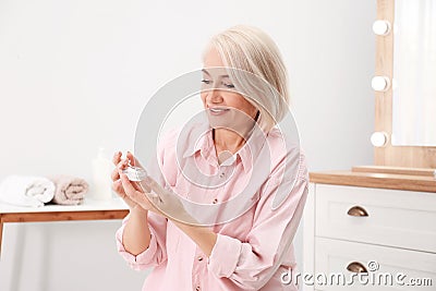 Portrait of charming mature woman with healthy beautiful face skin and natural makeup applying cream Stock Photo