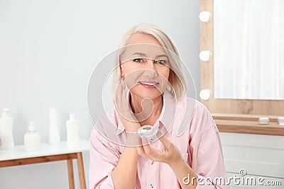 Portrait of charming mature woman with healthy beautiful face skin and natural makeup applying cream Stock Photo