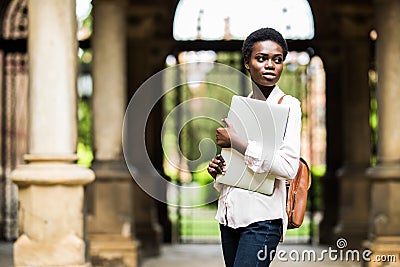 Time for study. Portrait of charming smiling young woman with laptop device in hands smiling at camera at campus. Cheerful afro am Stock Photo