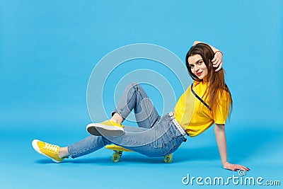 Portrait of charming young woman in vivid casual clothes looking camera and sitting with yellow skateboard isolated on Stock Photo