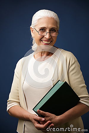 Portrait of cheerful aged woman in glasses, holding book, looking at camera Stock Photo