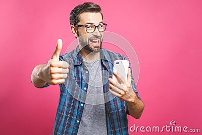 Portrait of a cheerful bearded man taking selfie and showing thumbs up gesture over pink background. Isolated Stock Photo