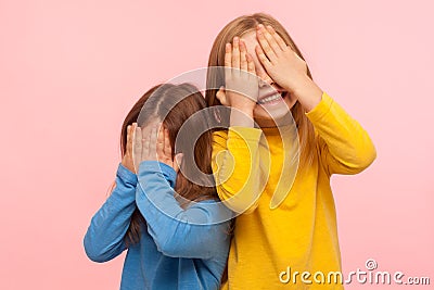 Portrait of cheerful joyful carefree little girls covering their faces with arms and sincerely smiling Stock Photo