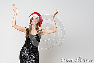 Portrait of a cheerful laughing woman in christmas hat and exquisite black dress while standing hands raised and looking at camera Stock Photo