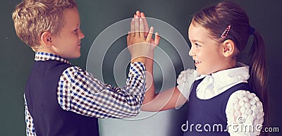 Portrait of cheerful little boy and girl playing together patty cake standing near the blackboard in the classroom. Stock Photo