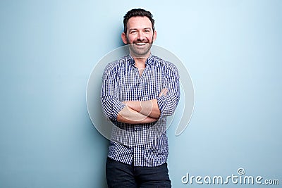 Cheerful man with beard posing against blue wall with arms crossed Stock Photo