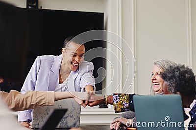 Portrait of cheerful multiracial LGBTQ mid adult woman fist bumping colleagues in meeting and smiling Stock Photo
