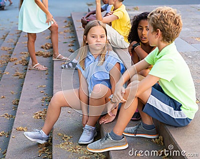 Cheerful preteen girls and boys sitting on steps outdoors and chatting Stock Photo