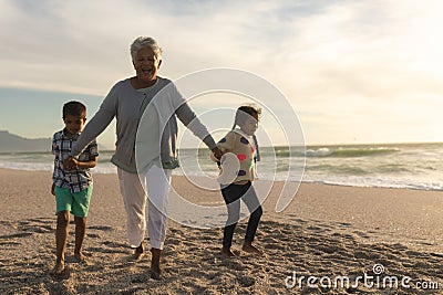Portrait of cheerful senior biracial woman holding hands with grandchildren while walking at beach Stock Photo