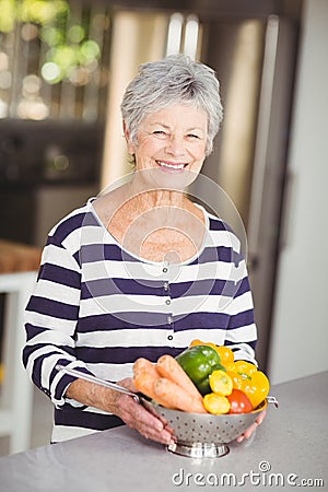 Portrait of cheerful senior woman holding colander with vegetables Stock Photo