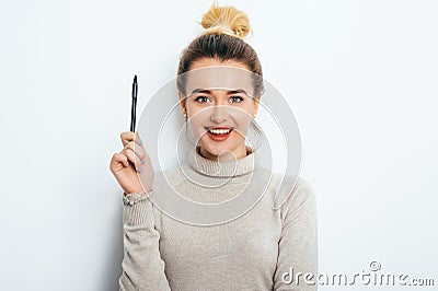 Portrait of cheerful woman with appealing smile, having hair bun in sweater isolated on white background holding pen and have a gr Stock Photo