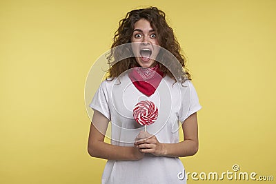 Portrait of cheerful woman holding a lollipop candy in the hand over yellow background Stock Photo