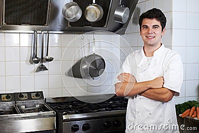 Portrait Of Chef Wearing Whites Standing By Cooker In Kitchen Stock Photo