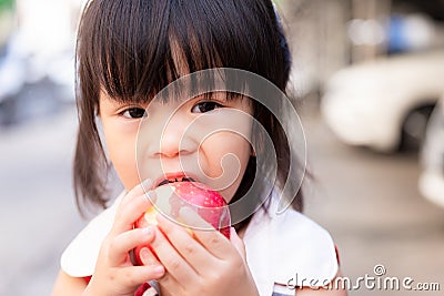 Portrait of child girl eating red apple and looking at camera. Head short of healthy kid eating fresh fruit for snack time. Stock Photo