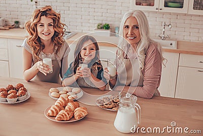 Portrait of child, woman and senior woman sitting at the kitchen table and holding glasses of milk Stock Photo