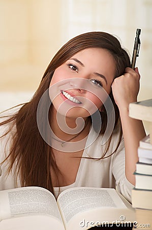 Portrait of clever student with open book reading it in college library holding a pen Stock Photo