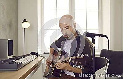 Concentrated talented male musician plucking strings on acoustic guitar creating new music. Stock Photo