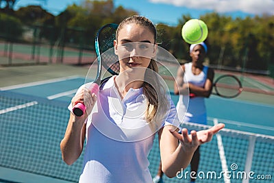 Portrait of confident female caucasian tennis player catching ball with african american competitor Stock Photo