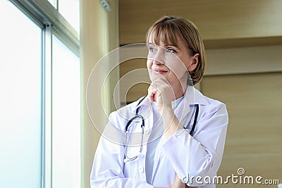 Portrait of confident female doctor in workwear with stethoscope thinking and taking decisions with hand on chin, looking through Stock Photo