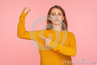 Portrait of confident ginger girl in sweater pointing at her biceps, showing power in hand and looking proudly, feeling strong Stock Photo