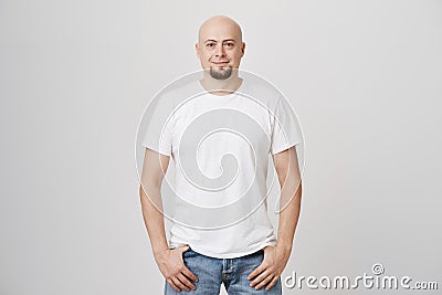 Portrait of confident good-looking bald caucasian guy wearing casual t-shirt and jeans, holding hands in pockets Stock Photo