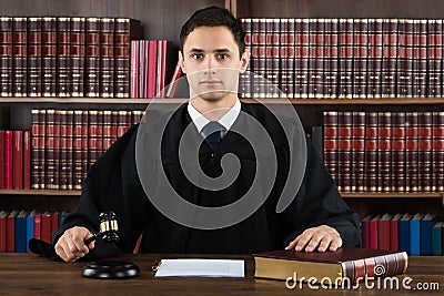 Portrait Of Confident Judge Hitting Mallet At Desk Stock Photo