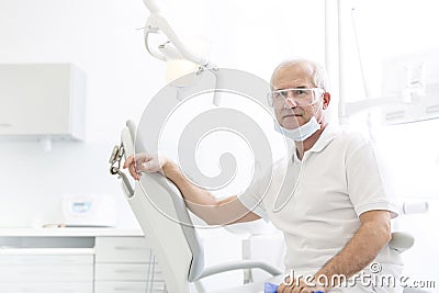 Portrait of confident senior dentist sitting on chair at dental clinic Stock Photo