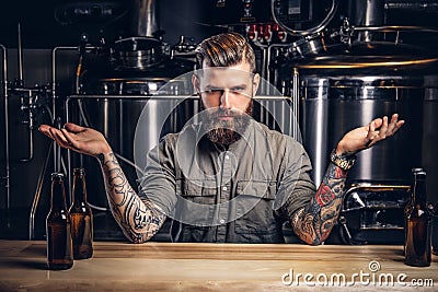 Portrait of a confident tattooed hipster male with stylish beard and hair in shirt in the indie brewery. Stock Photo