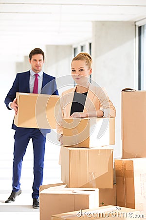 Portrait of confident young businesswoman standing by stacked boxes with male colleague in background at office Stock Photo