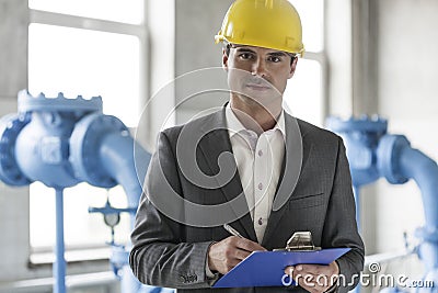 Portrait of confident young male supervisor writing on clipboard in industry Stock Photo