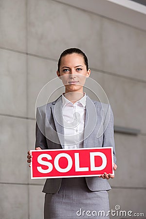 Portrait of confident young saleswoman holding sold placard while standing against wall in apartment Stock Photo