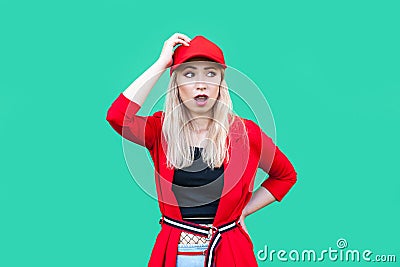 Portrait of confused blond young hipster woman in red blouse, cap, standing with hand on waist and on head looking away shocked, Stock Photo